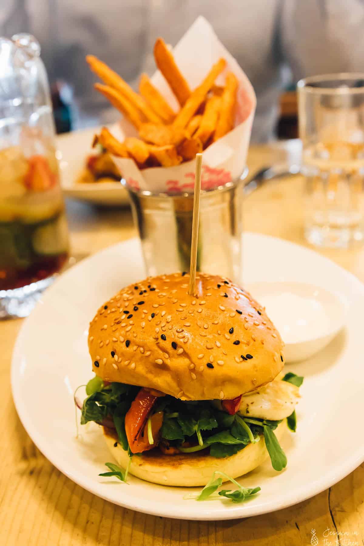 Burger on a plate with fries in the background. 