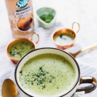 A cup of matcha latte in front of a bottle of almond creamer.