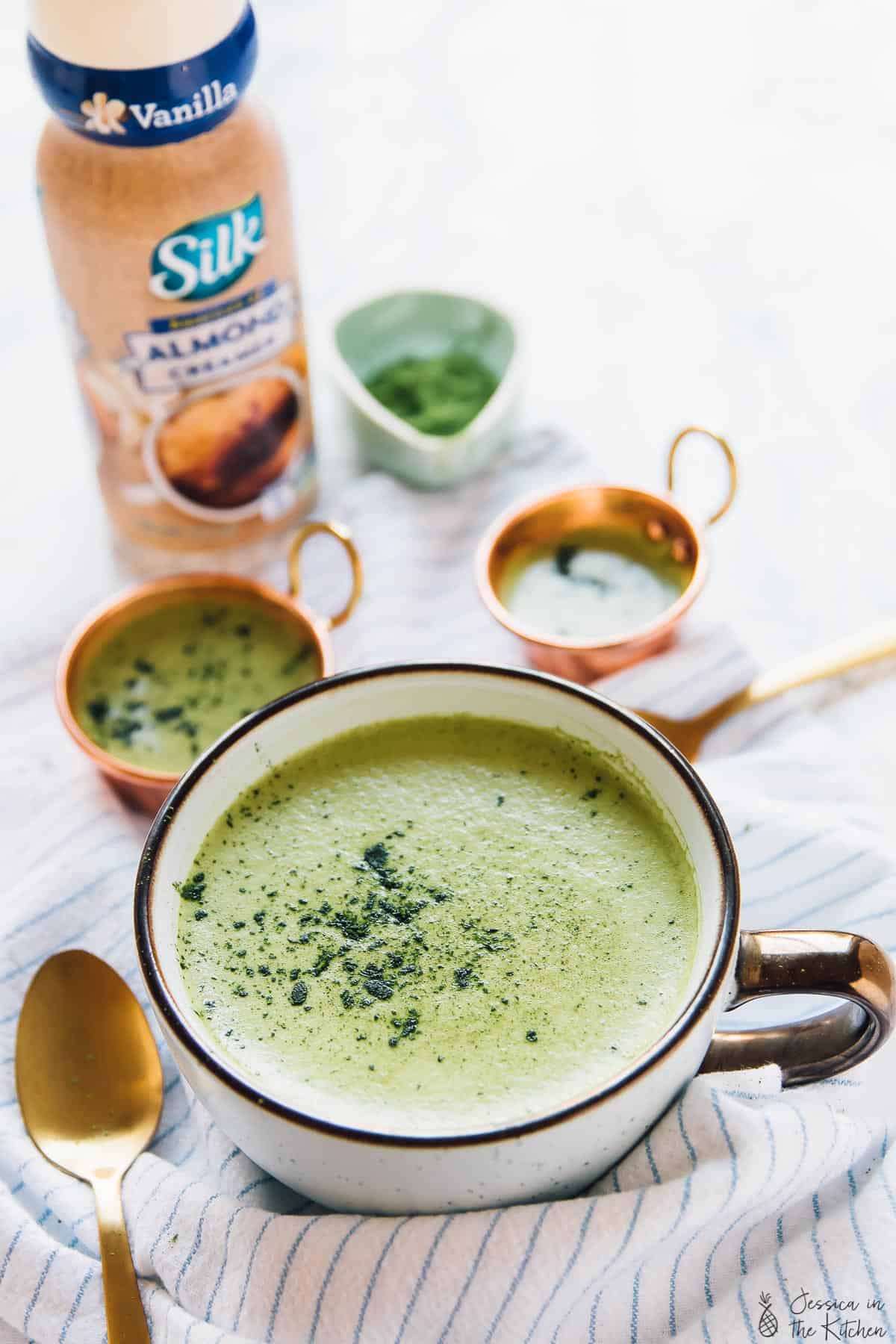 Pumpkin matcha latte in a white cup with a bottle of almond milk in the background. 