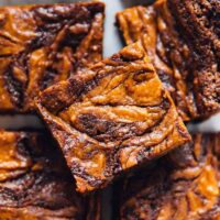 A top down view of a batch of vegan Pumpkin Cheesecake Swirl Brownies on a white table.