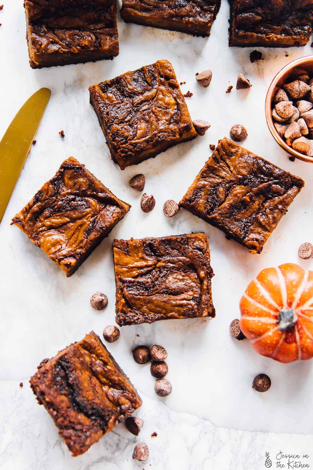 Overhead view of five brownie squares with cheesecake swirls next to chocolate chips