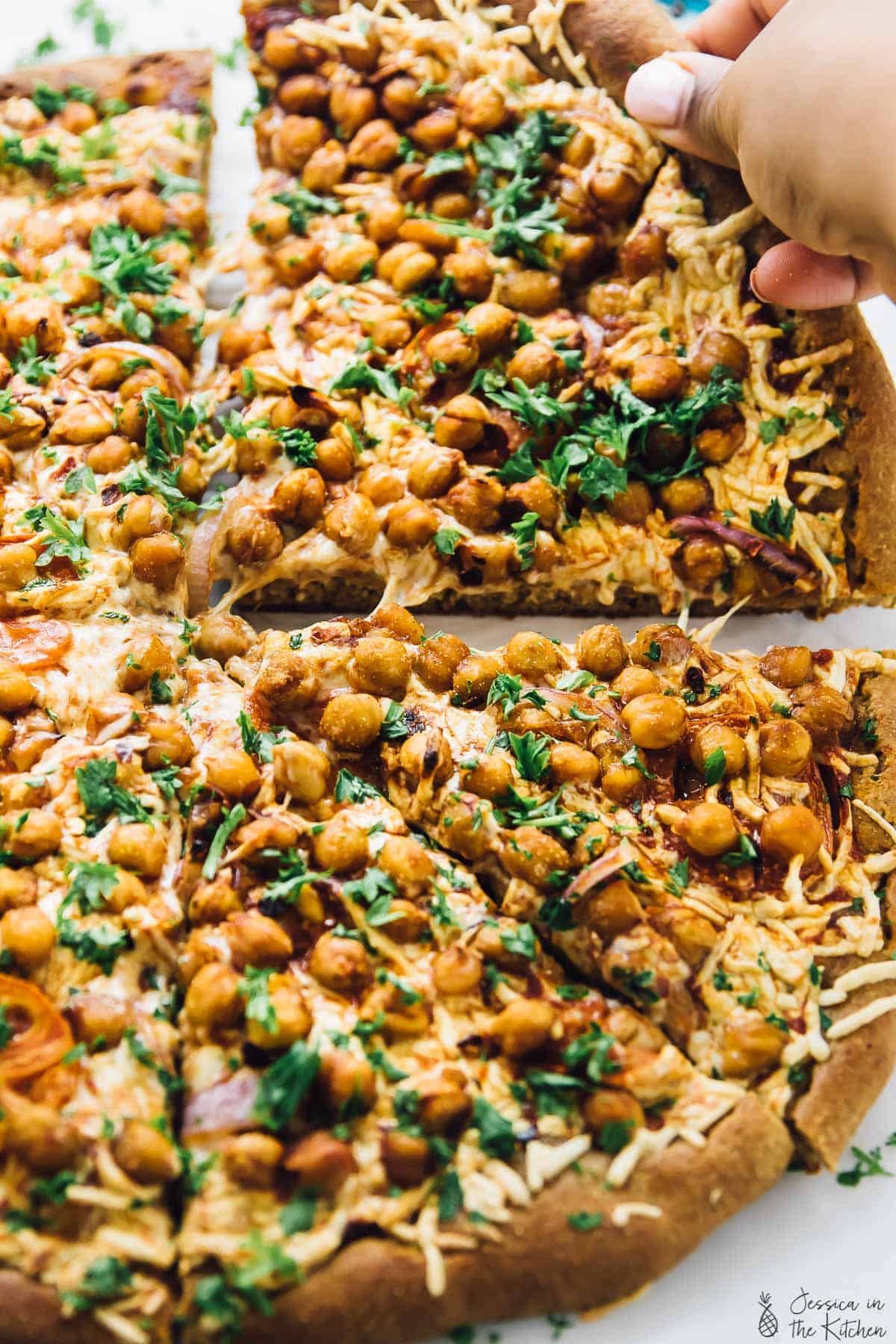 Hand pulling away slice of spicy BBQ chickpea pizza