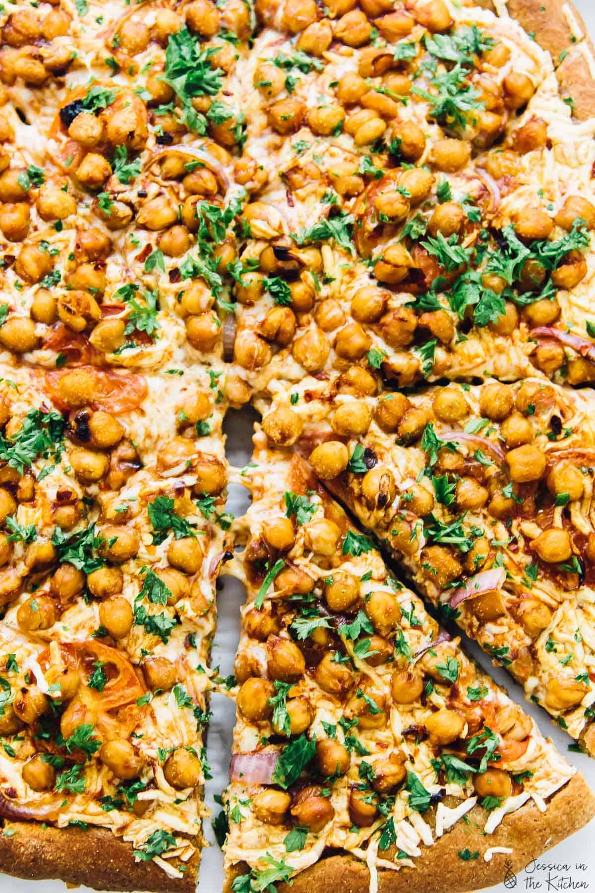 Overhead view of whole spicy BBQ chickpea pizza with one slice pulled away slightly