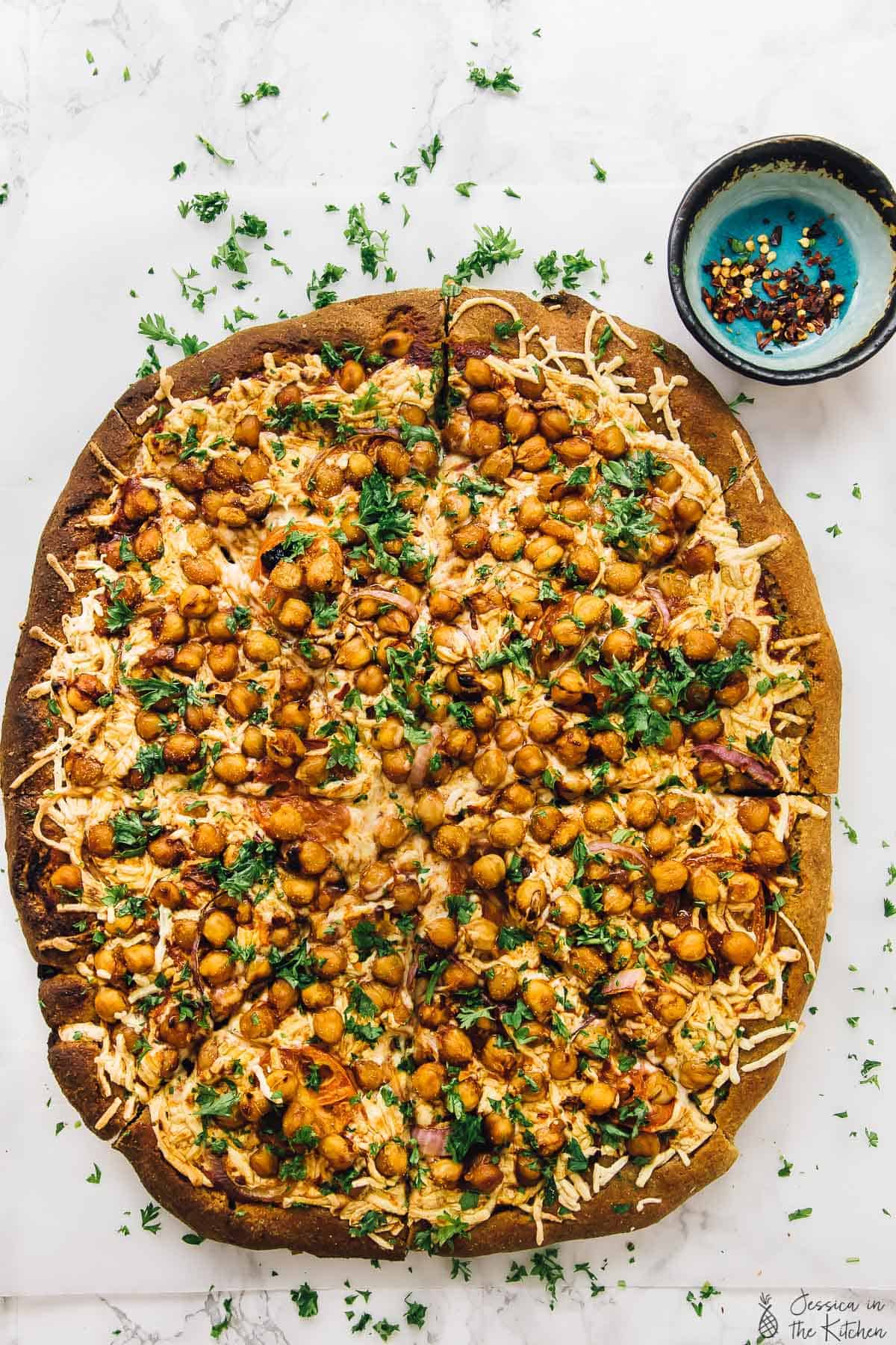 Overhead view of sliced BBQ chickpea pizza on parchment-lined baking sheet with parsley for garnish