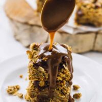 A spoon drizzling caramel sauce vegan apple pie bars.