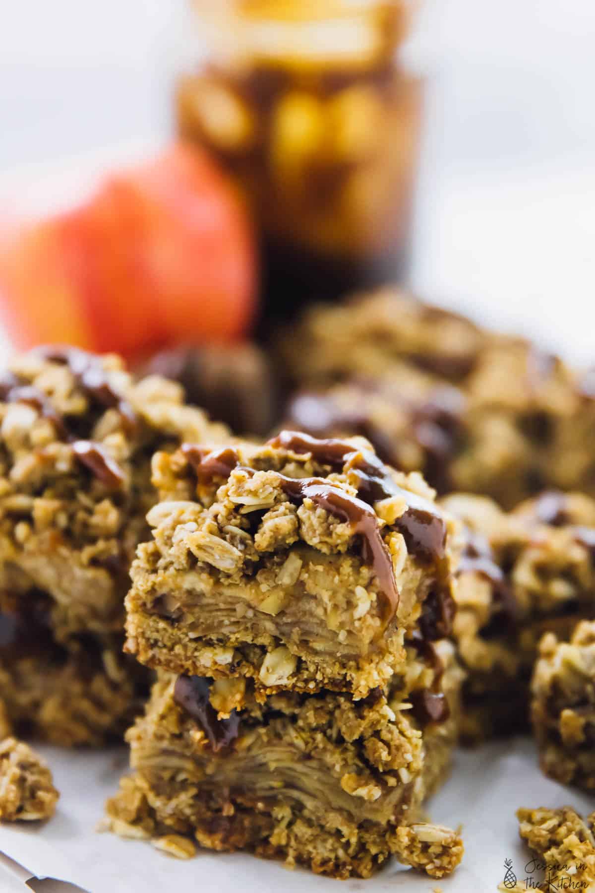 A close up of a batch of vegan apple pie bars with an apple in the background. 