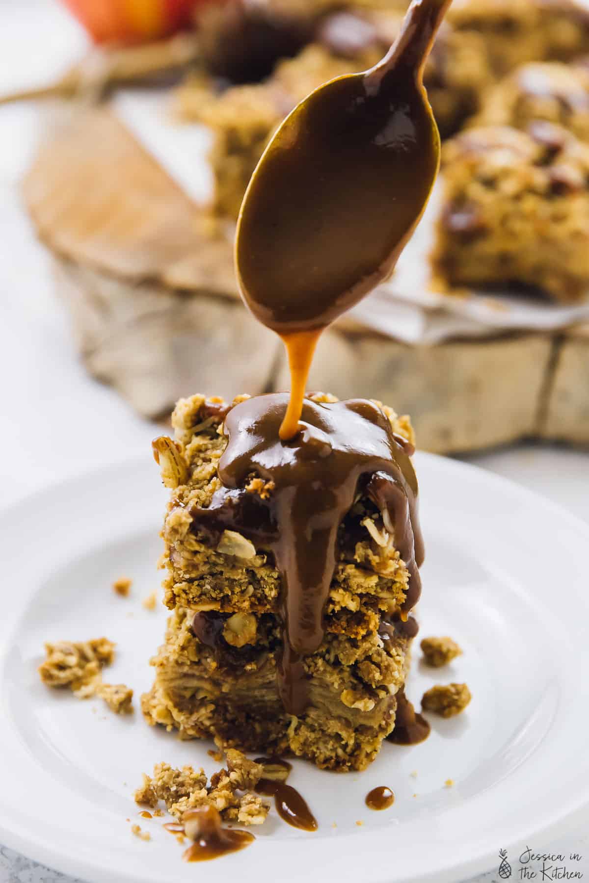 A spoon drizzling caramel sauce on a stack of apple pie bars.