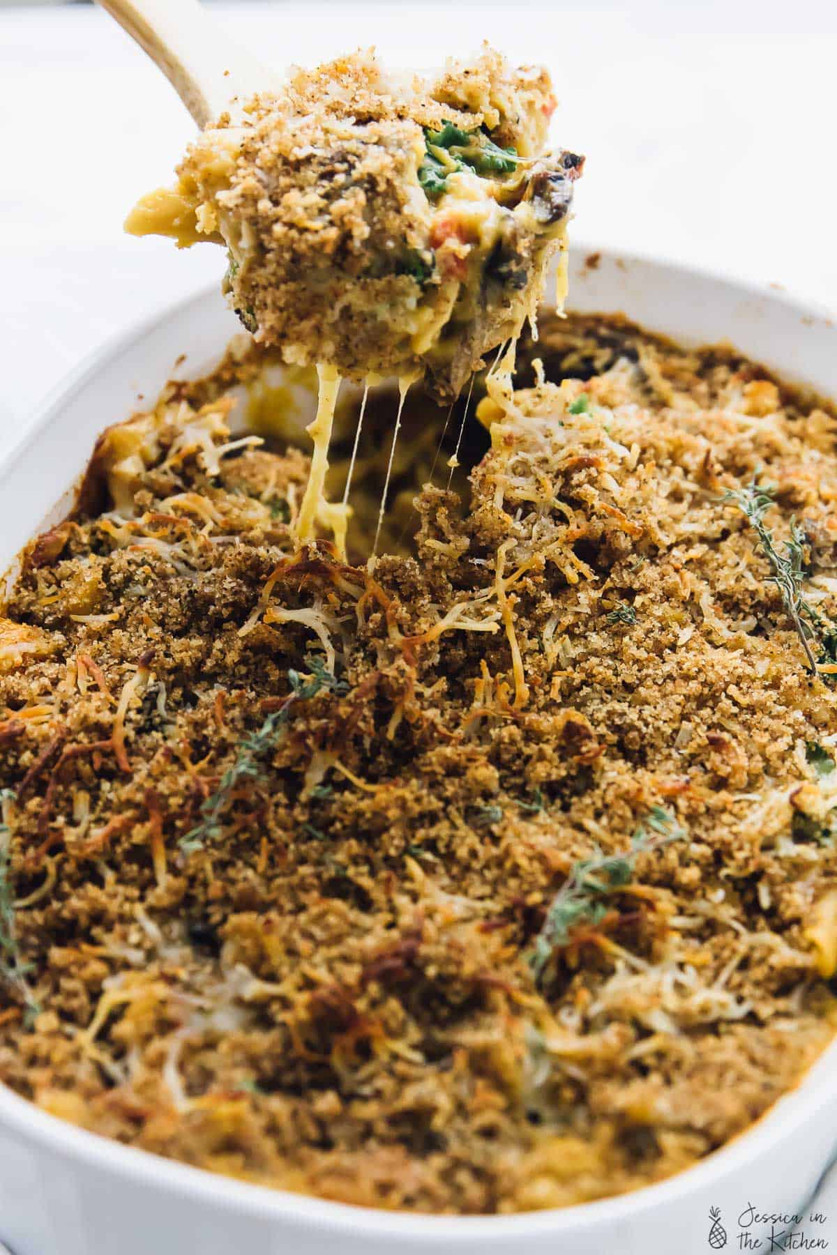 Spoon scooping up butternut squash pasta bake from a white baking dish.