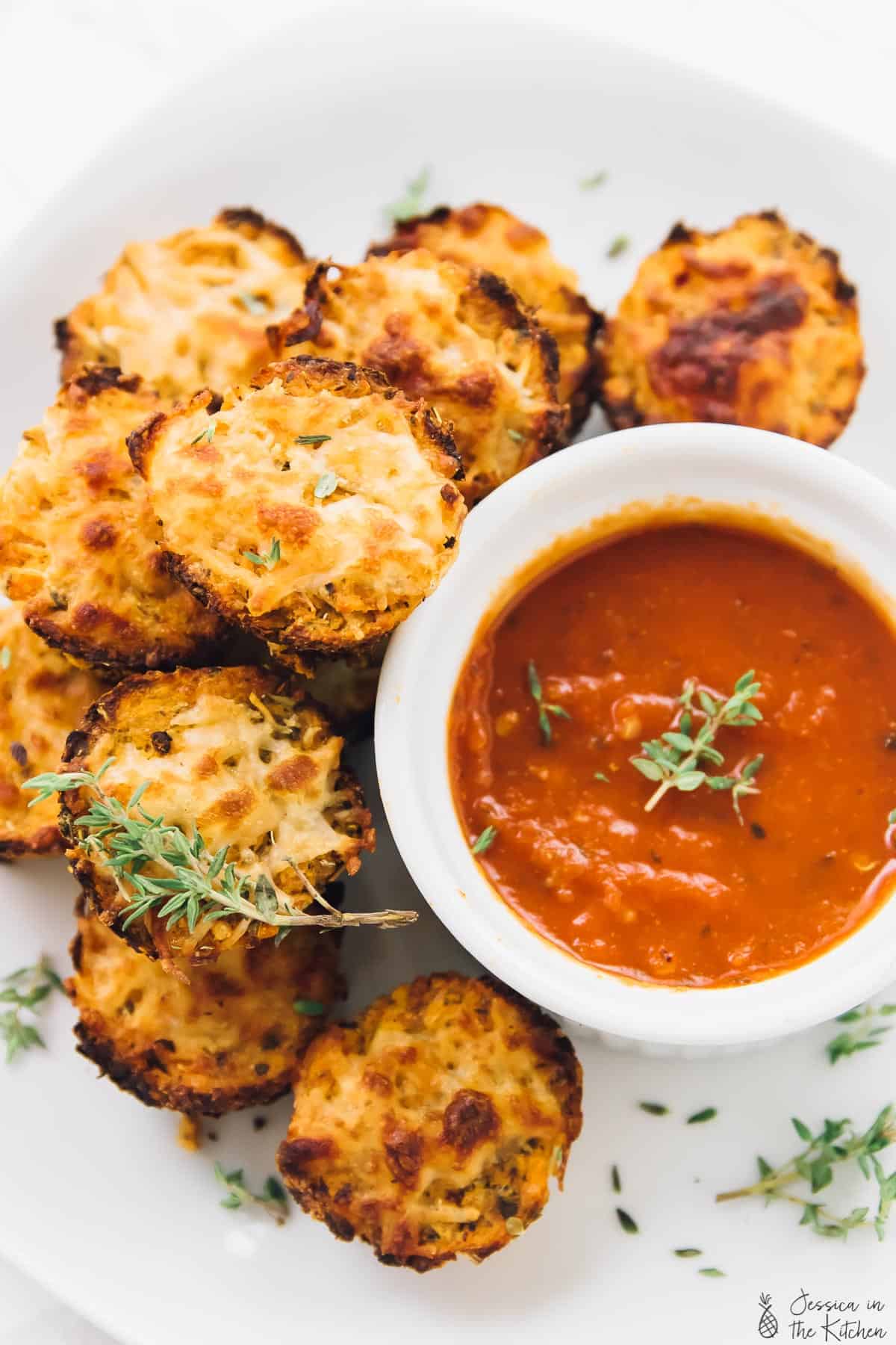 Cauliflower pizza bites next to a bowl of tomato sauce. 