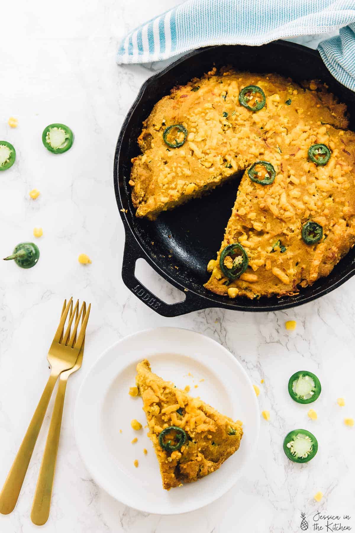 Top down view of cheesy cornbread in a skillet with a portion cut out. 