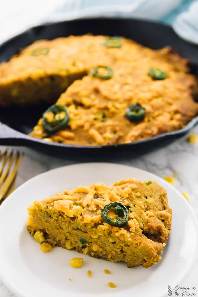 a slice of cornbread in front of a skillet of cornbread.