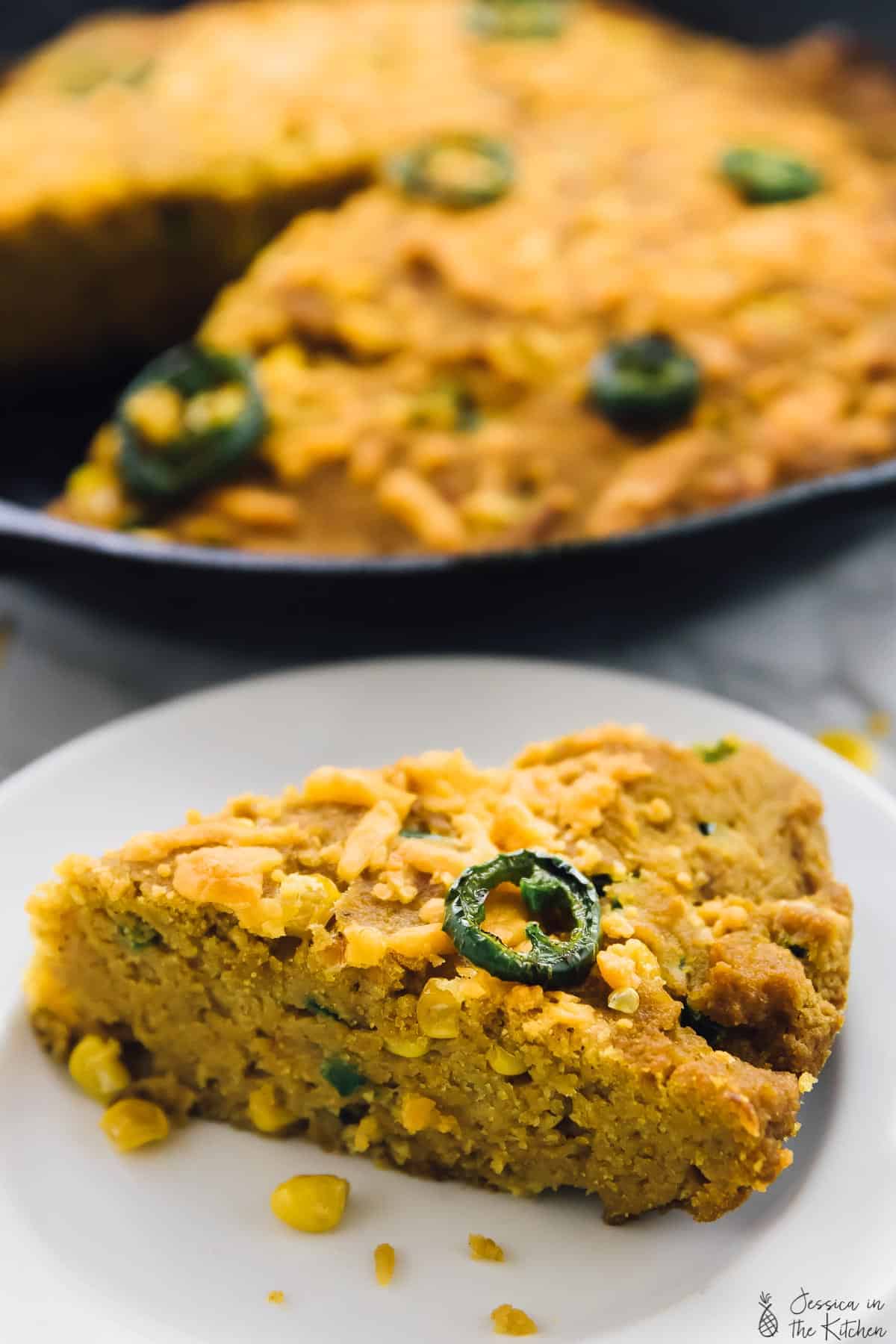 A close up of a slice of cornbread with a skillet of cornbread in the background. 