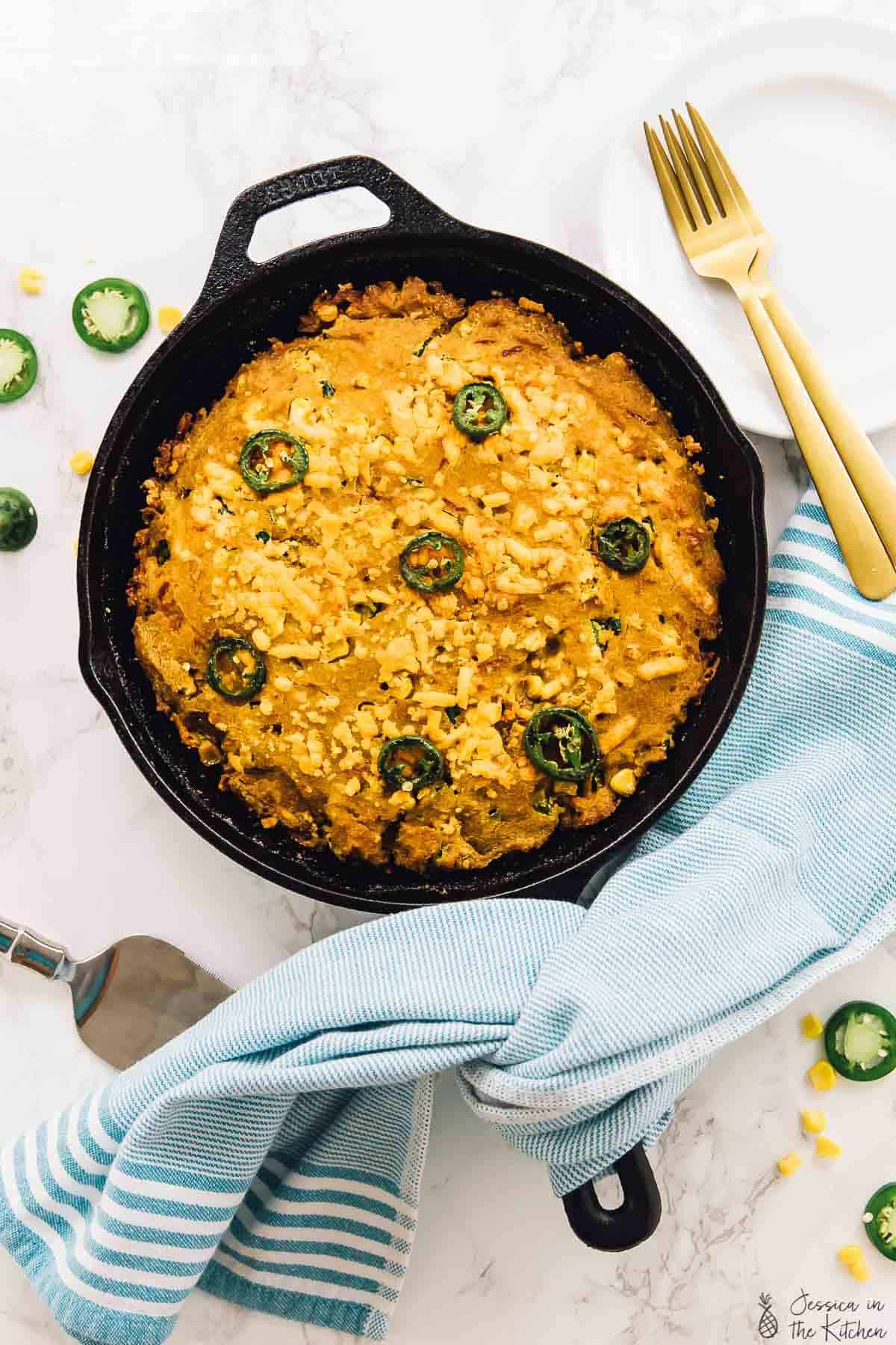 Top down view of cheesy cornbread skillet with gold forks on the side. 