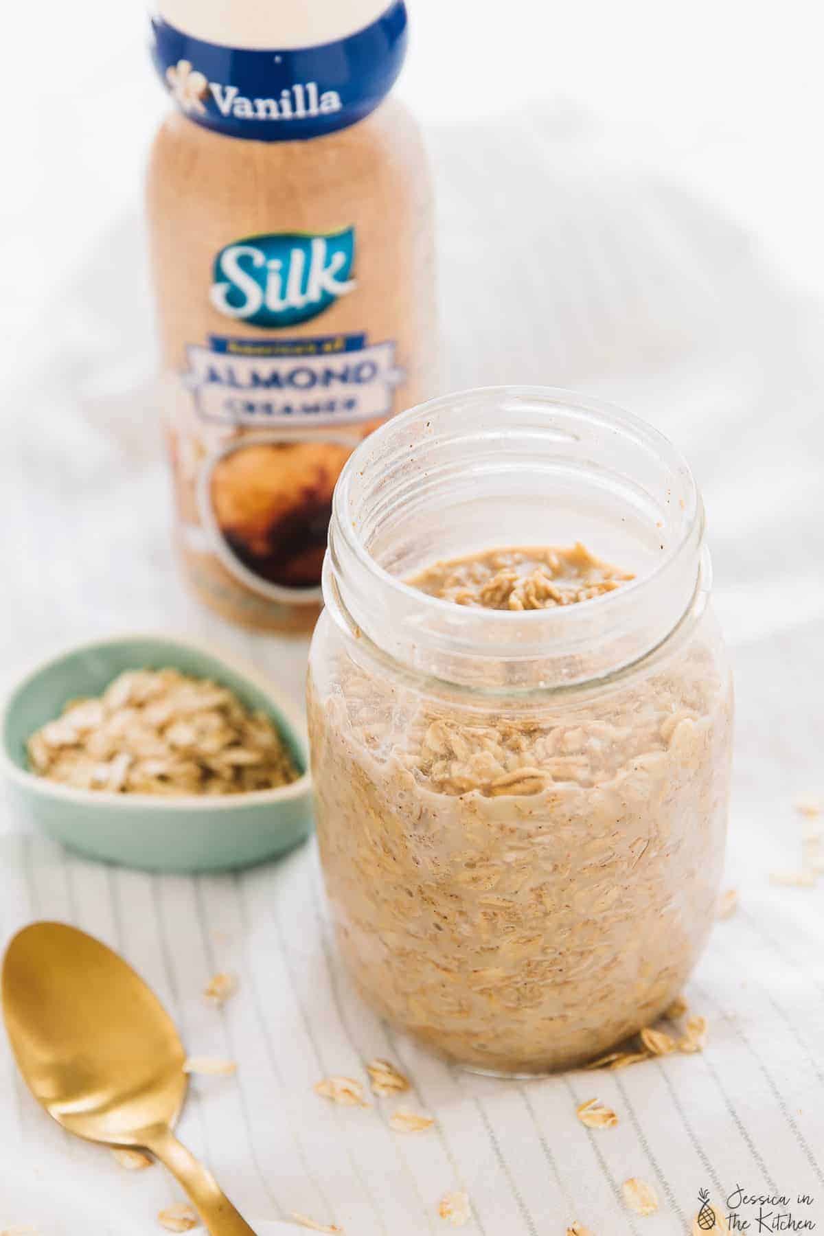 Espresso cinnamon overnight oats in a glass jar with a bottle of almond creamer in the background. 