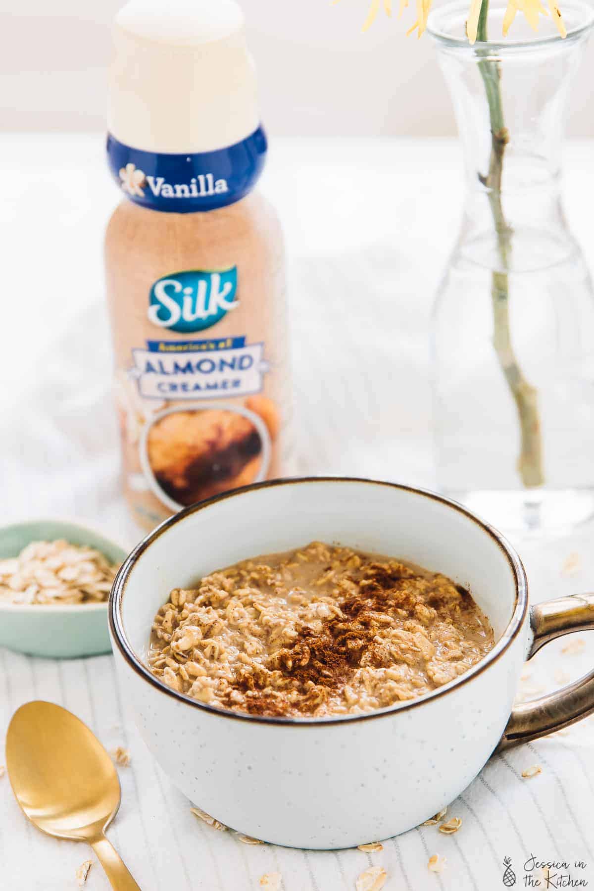 Espresso cinnamon overnight oats in a white cup with almond creamer in the background. 