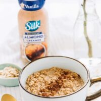 Overnight Oats in a white cup with a bottle of almond creamer in the background.