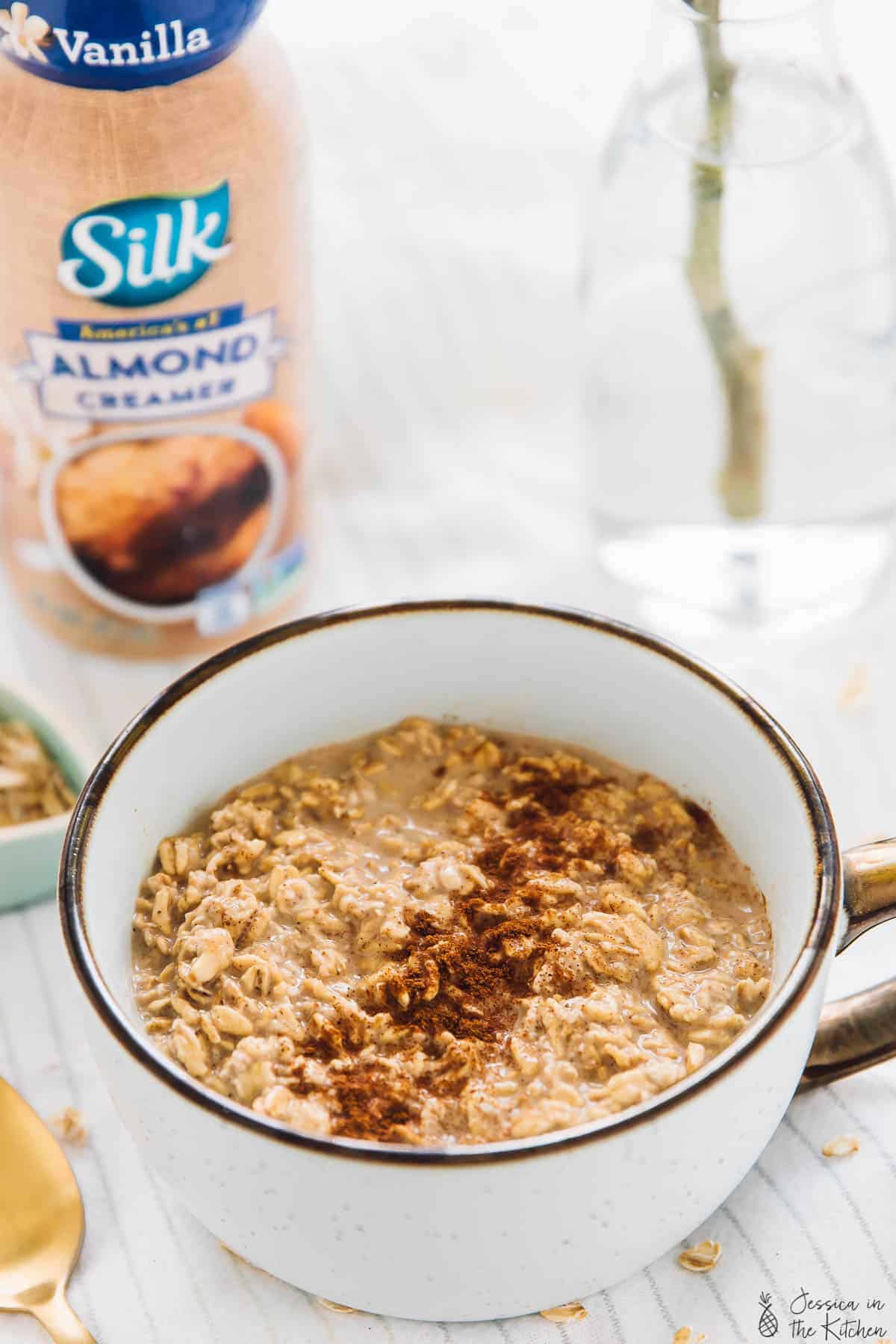 Cinnamon overnight oats in a white cup with almond creamer in the background. 