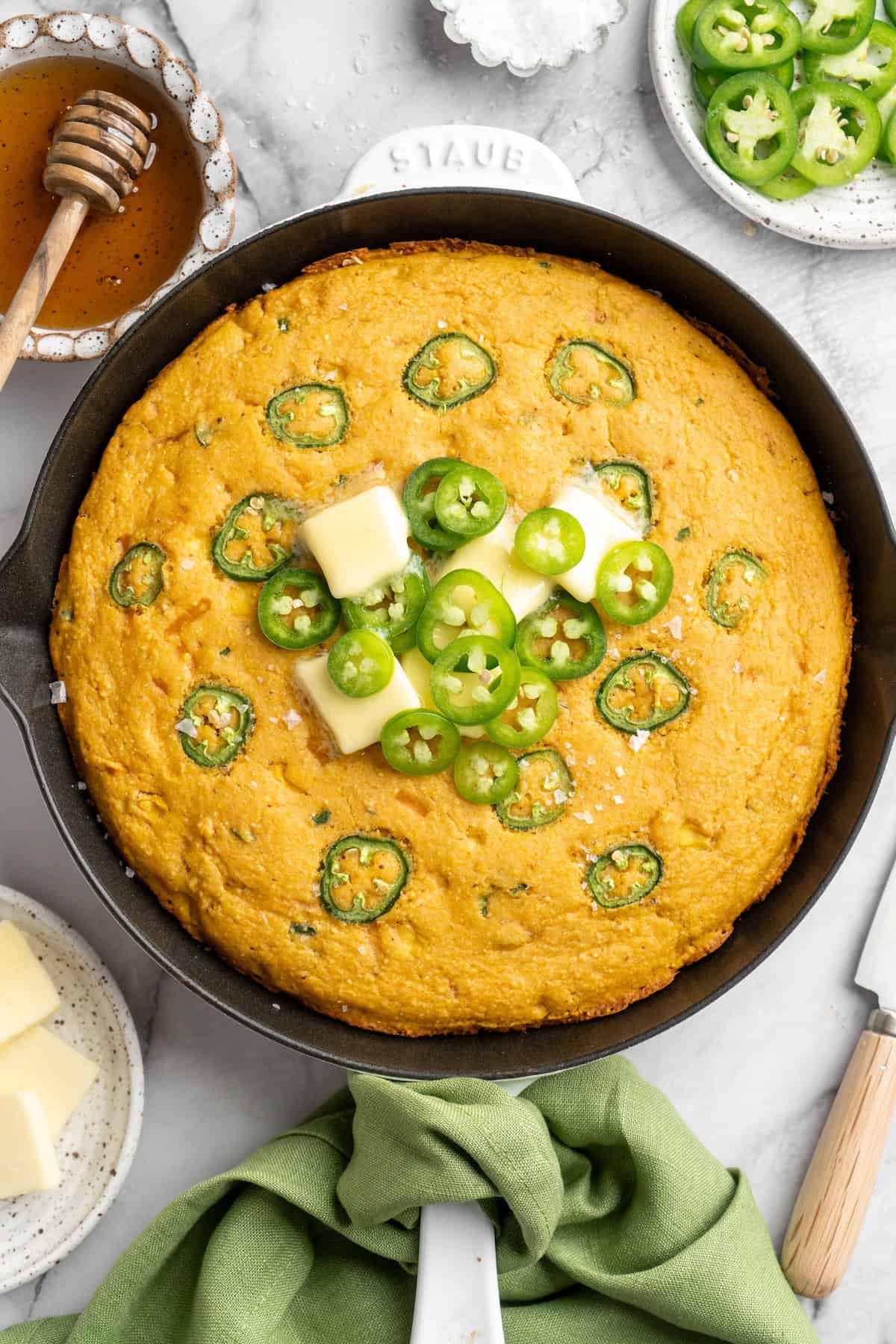 Pumpkin cornbread in skillet topped with vegan butter and jalapeños