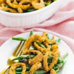 Green bean casserole on a plate with fork beside and rest of casserole in background.