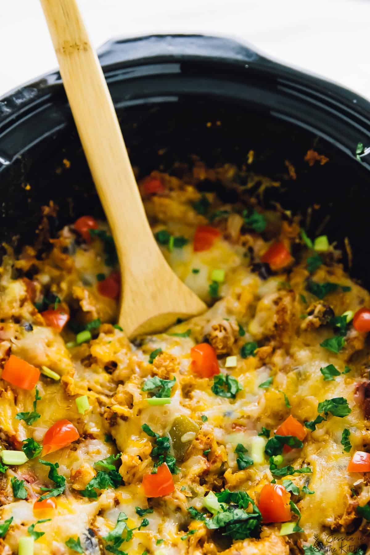 Wood spoon stirring quinoa enchilada casserole in a slow cooker. 