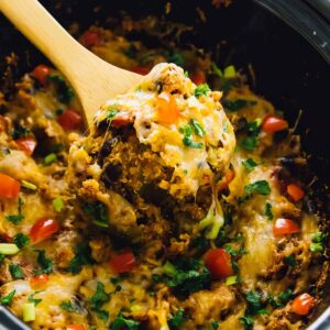 Quinoa enchilada casserole in a slow cooker, being stirred by a wood spoon.