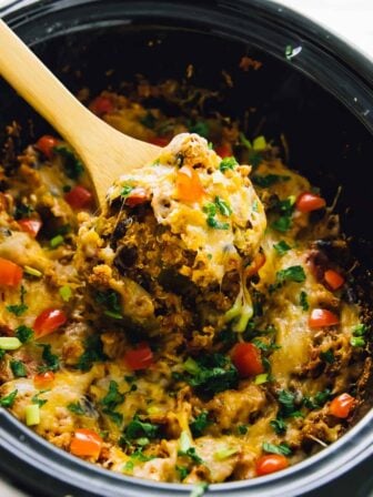 Quinoa enchilada casserole in a slow cooker, being stirred by a wood spoon.
