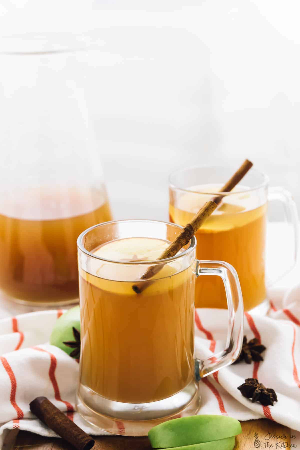 Two glass mugs of warm apple cider on a striped cloth.