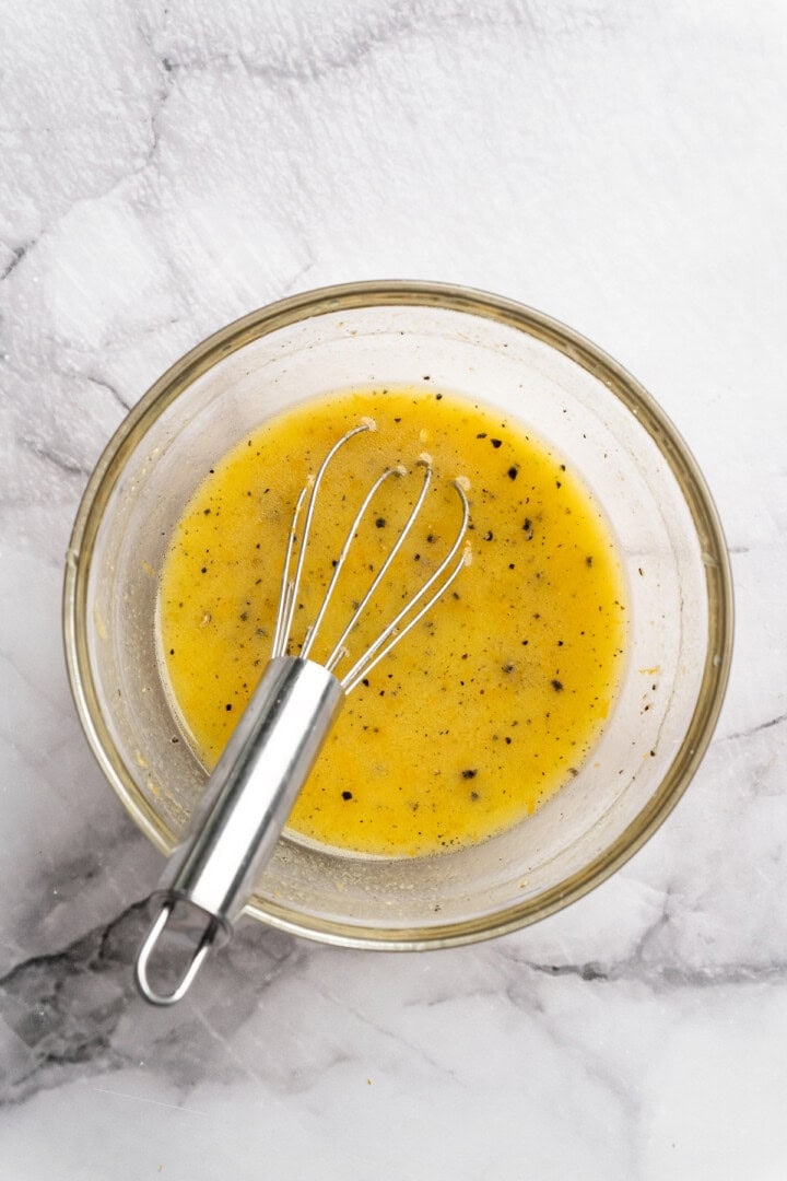 Orange vinaigrette in glass bowl with small whisk.