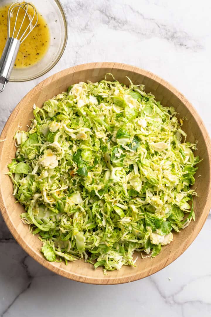 Shaved Brussels sprouts in large serving bowl next to small bowl of orange vinaigrette.