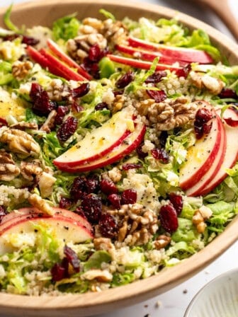 Shaved Brussels sprout salad with apples, walnuts, and cranberries in serving bowl.