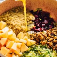 Pouring vinaigrette onto a salad in a brown bowl.