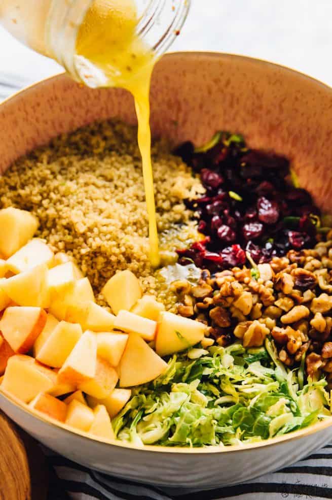 Pouring vinaigrette onto a salad in a brown bowl.