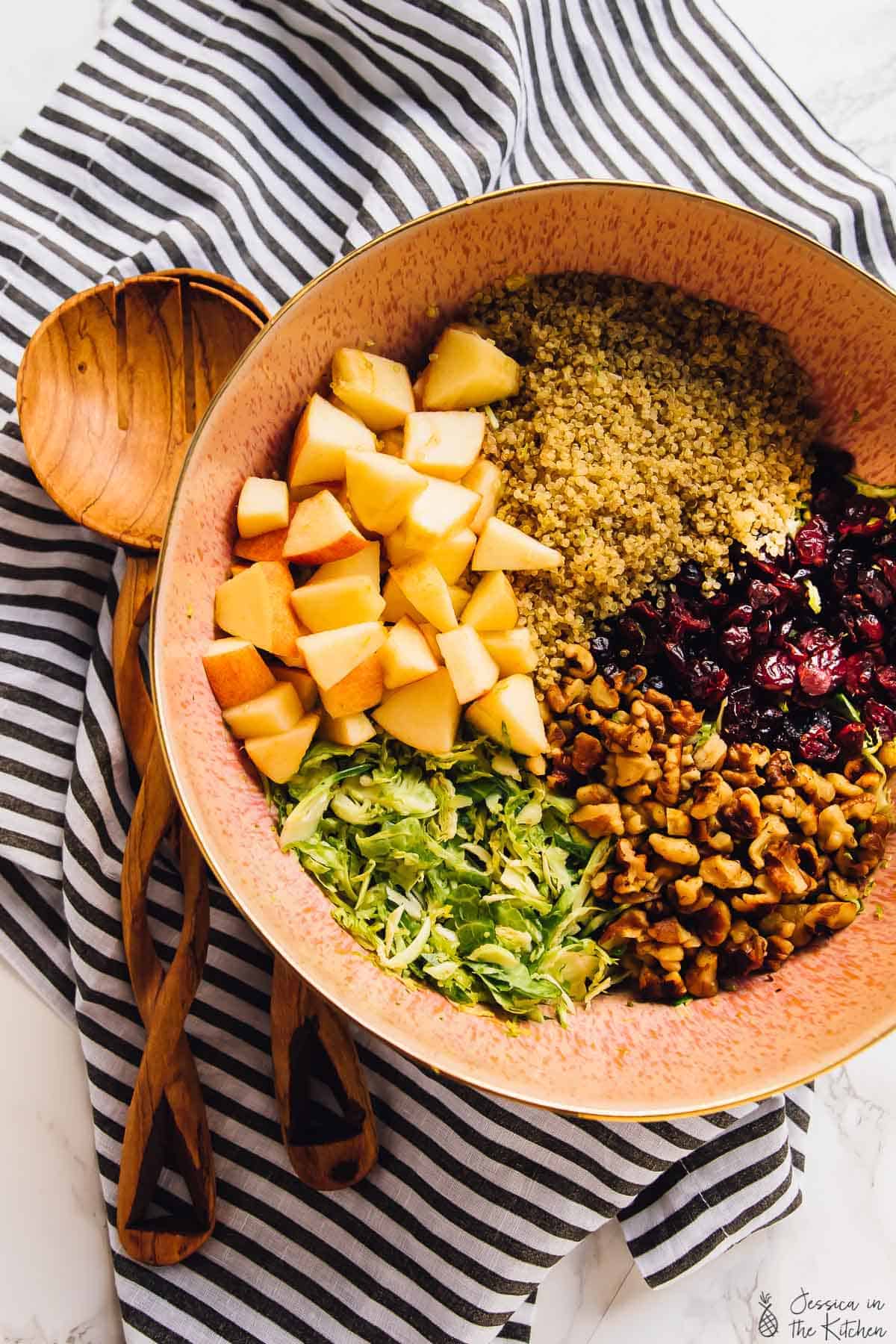 Top down view of shaved sprouts, cranberries, nuts and quinoa in a brown bowl. 