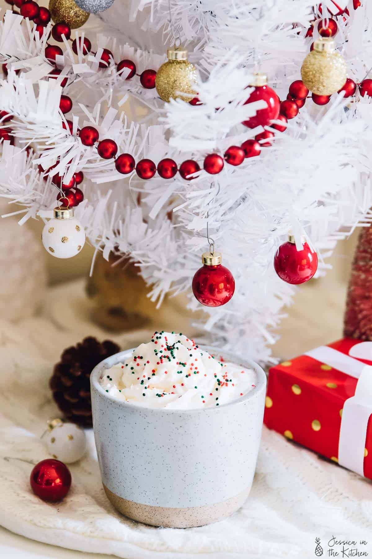 Hot chocolate in a grey cup under a white christmas tree. 