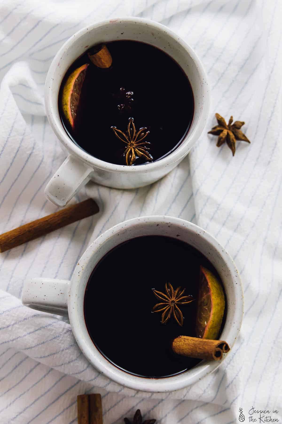 Overhead view of mulled wine in two mugs with cinnamon sticks and star anise. 