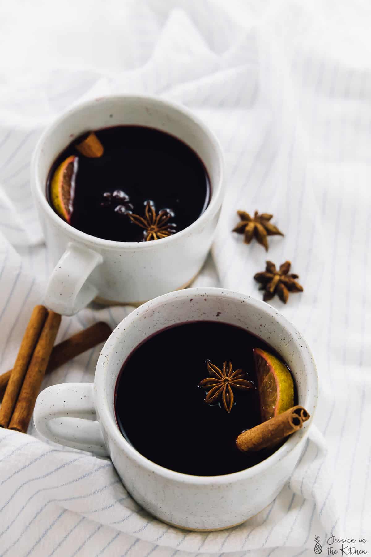 Two mugs of spiced mulled wine on a striped cloth. 