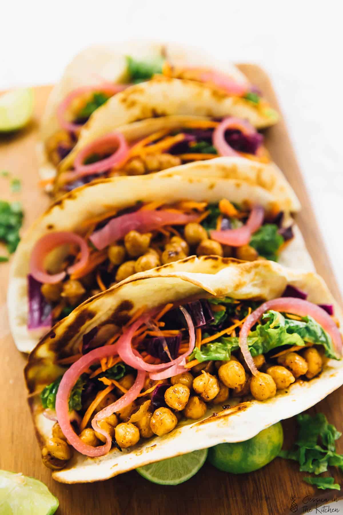 4 vegan BBQ chickpea tacos on cutting board, topped with pickled onions and slaw