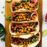 Overhead view of four BBQ chickpea tacos lined up on wooden cutting board