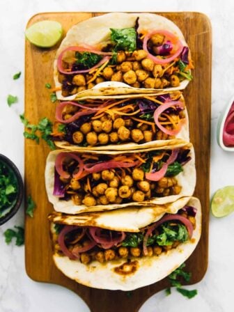 Overhead view of four BBQ chickpea tacos lined up on wooden cutting board