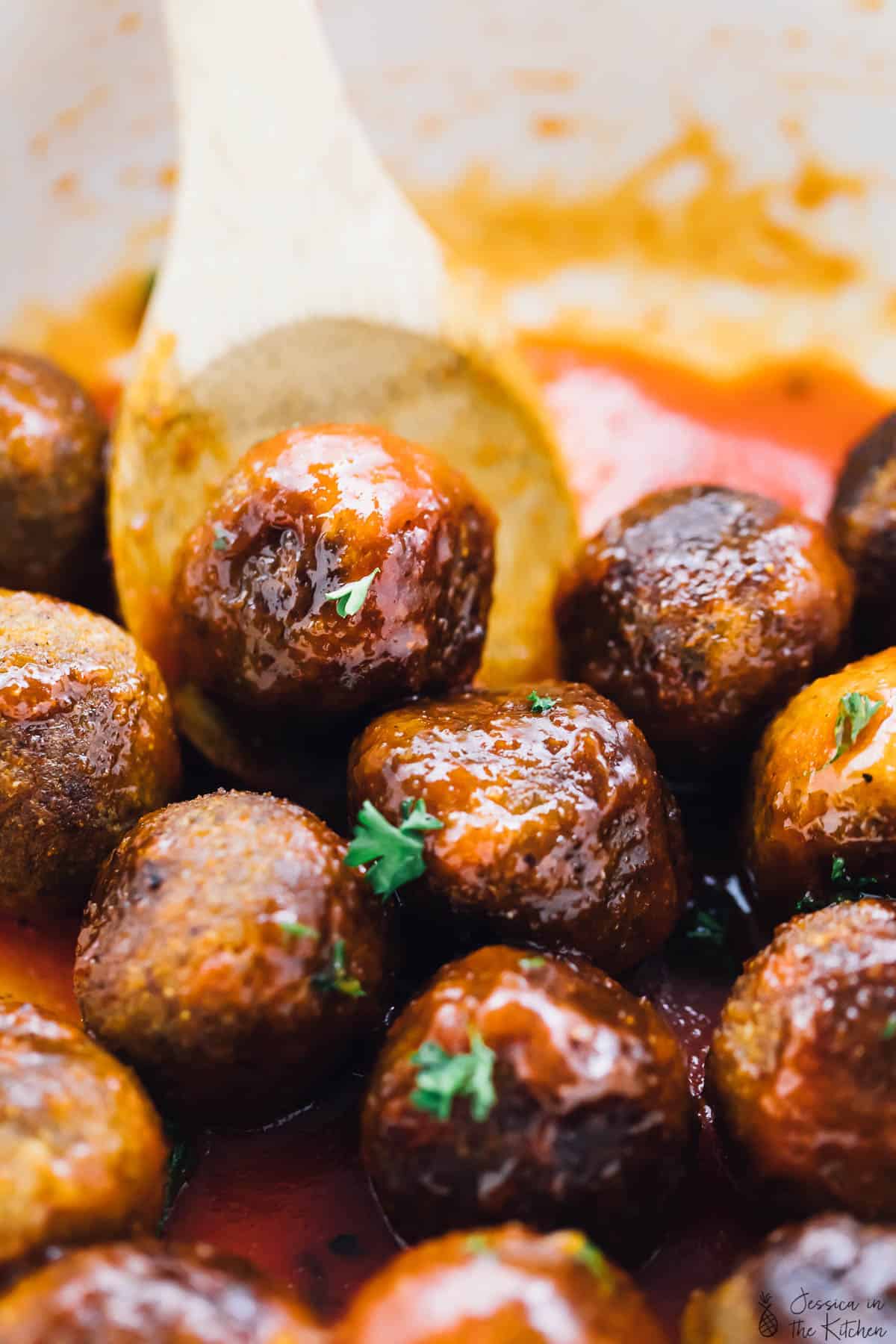 Vegan meatballs being stirred in a pot with a wood spoon. 