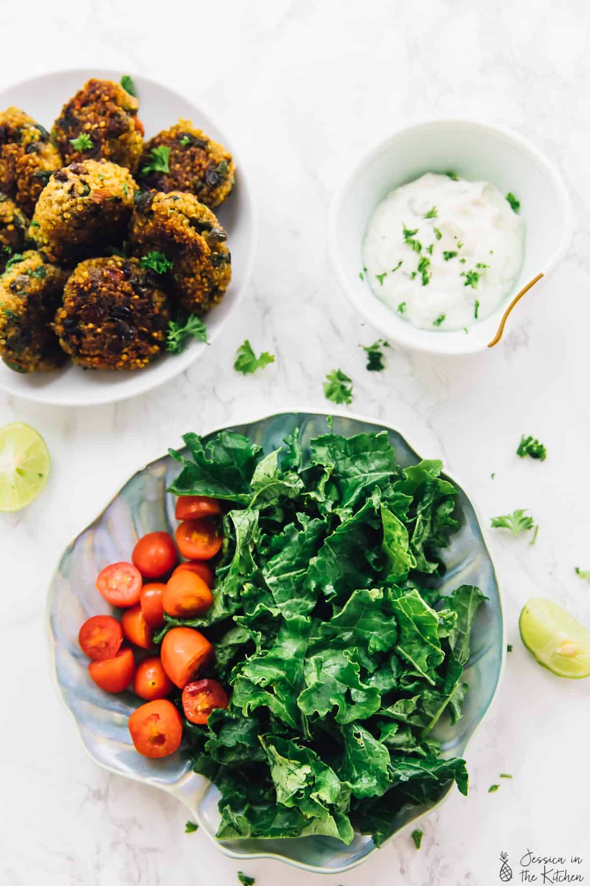 Overhead view of bowl of quinoa patties, bowl of tahini yogurt sauce, and plate of greens and tomatoes