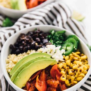 Two Mexican street corn burrito bowls on a striped cloth