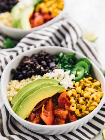 Two Mexican street corn burrito bowls on a striped cloth