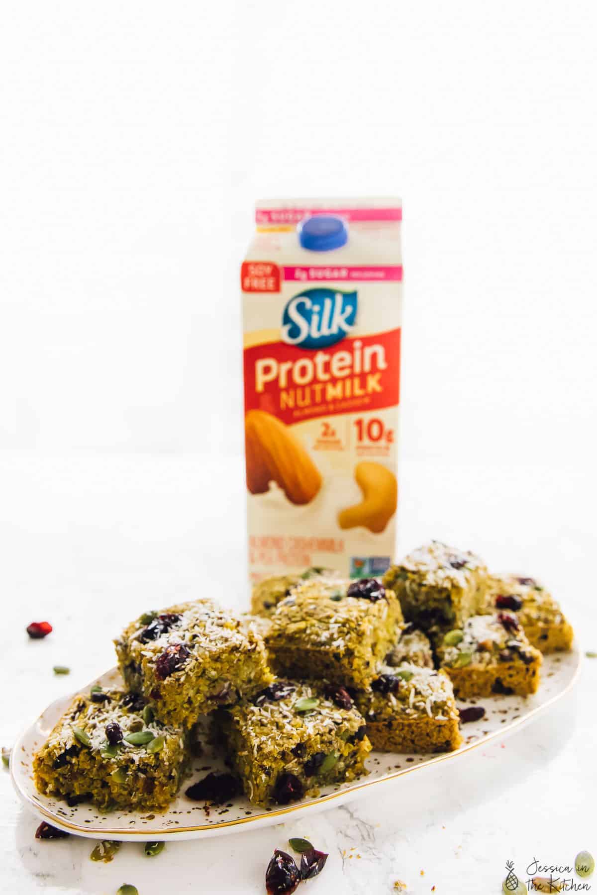 Breakfast bars on a plate with a carton of nut milk in the background. 