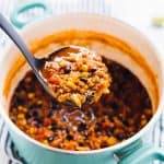 a pot of red lentil chili in a ladle over a larger blue pot of chili