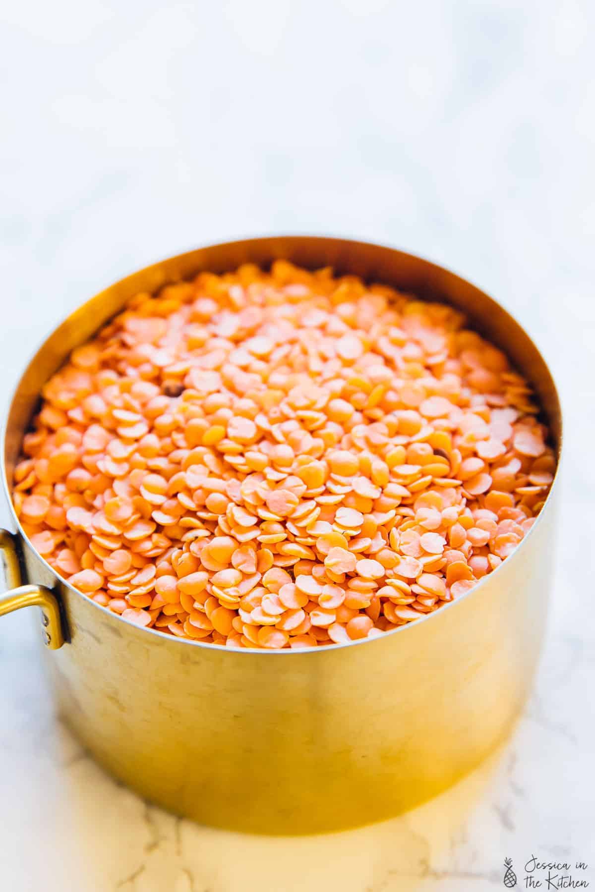 A gold sauce pot of raw red lentils on a white granite countertop