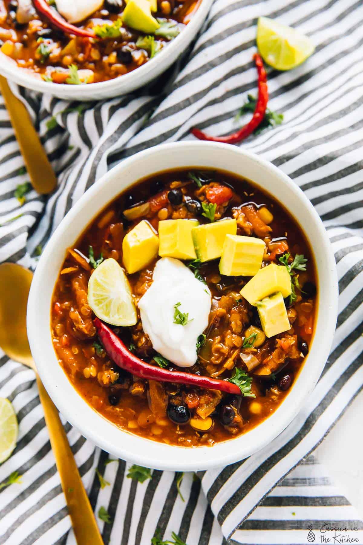 Overhead view of red lentil chili in a bowl, topped with diced avocado and sour cream.