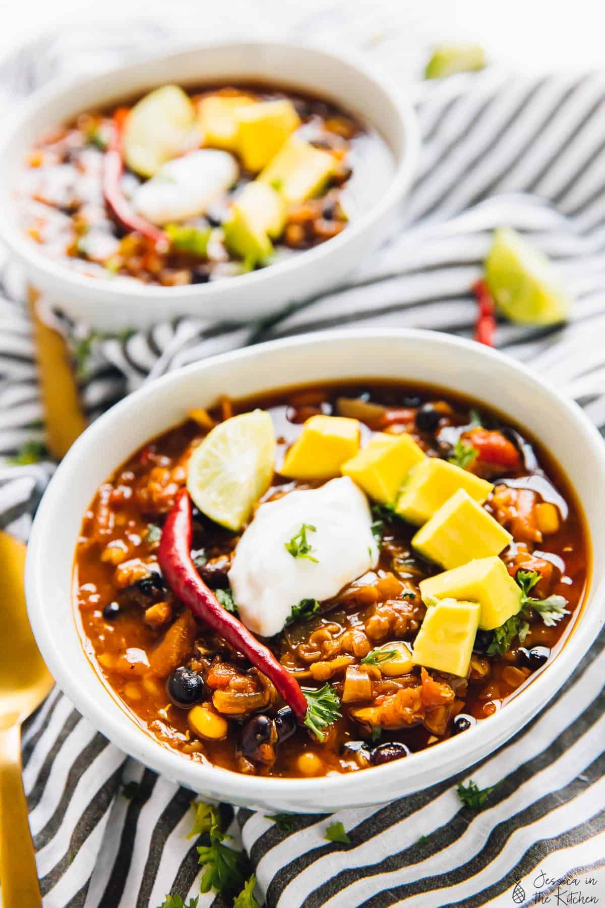 Close up of red lentil chili in two white bowls, on a striped cloth. 