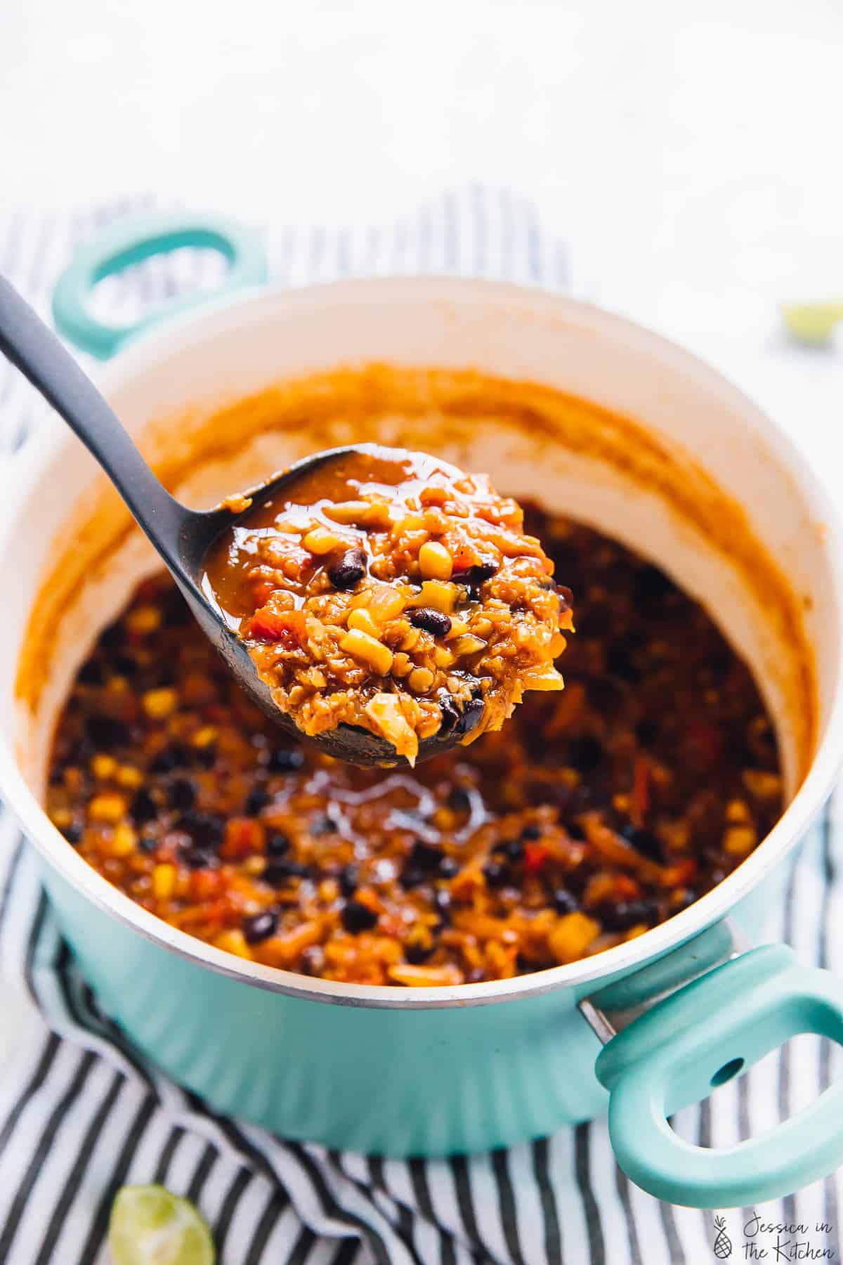 A ladle with some lentil chili, over a pot of lentil chili.