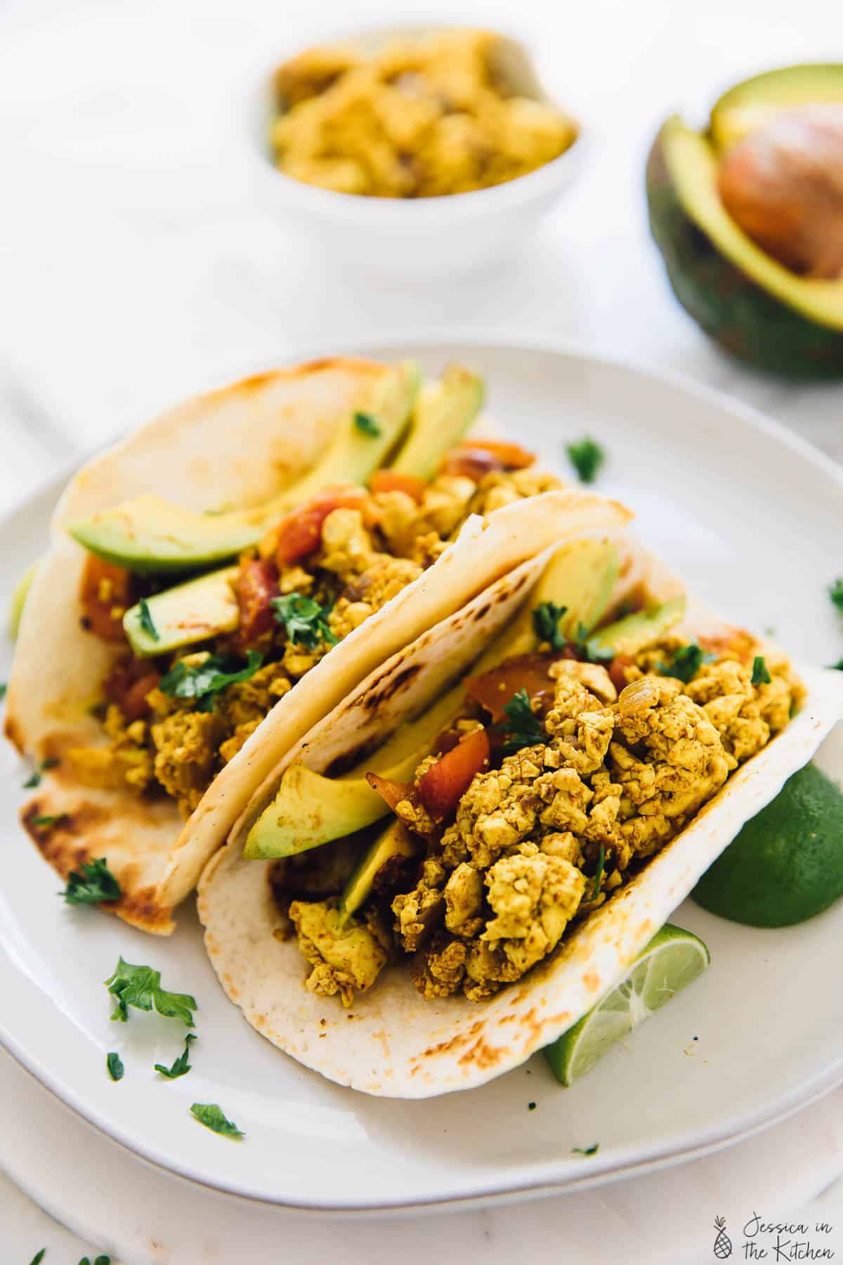 Two tofu scramble breakfast tacos with lime wedges on the side. 